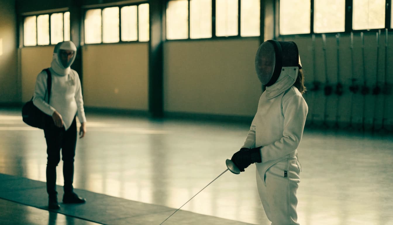 A fencing instructor and a student in protective gear and masks practicing in a bright studio.